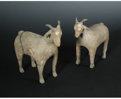A pair of Han dynasty grey pottery goats, each characterful figure standing four square, its eyes and nostrils painted white,