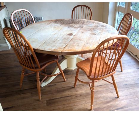 A large circular form, beige kitchen table and a set of five traditional style hoop stick back Windsor chairs.