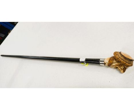 An ebonised walking stick with carved antler finial in the form of a caricature head, 88cm.