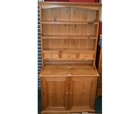 A 20th century pine country kitchen dresser, outswept cornice above three plate racks and three short drawers, the protruding