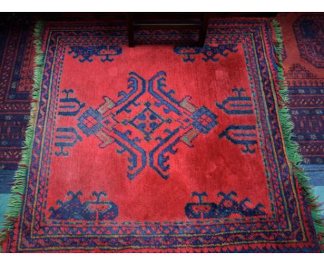 An Oriental carpet, in tones of blue and green on a red ground, 110cm x 110cm