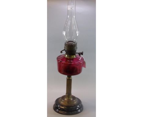 Early 20th century double burner oil lamp, having cranberry glass reservoir on a brass and ebonised base. (B.P. 21% + VAT) Sm