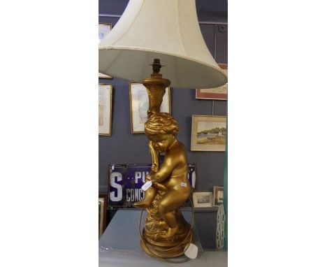 Modern gilded finish table lamp in the form of a seated cherub on scroll decorated base, with shade.  (B.P. 21% + VAT) 