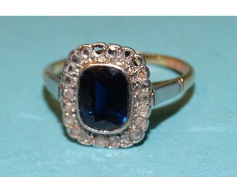 An Edwardian sapphire and diamond cluster ring, the cushion-cut sapphire within a border of nineteen rose-cut diamonds, (two 