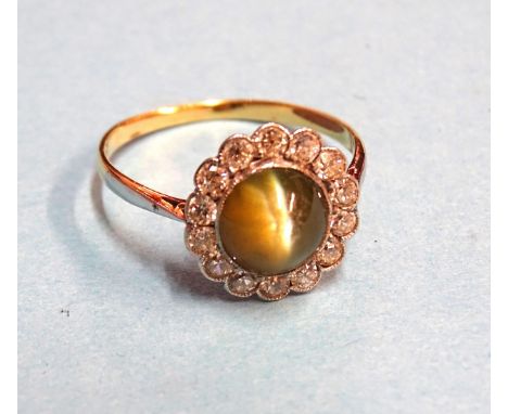 An Edwardian chrysoberyl cat’s eye and diamond cluster ring collet-set a round chrysoberyl within surround of fourteen Swiss-