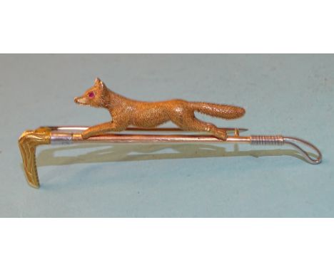 An Edwardian gold hunting brooch in the form of a running fox with inset ruby eyes, on a yellow, white and rose gold riding c