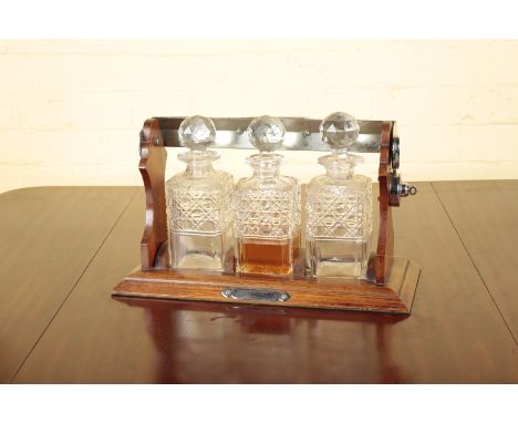 AN OAK THREE BOTTLE TANTALUStogether with three cut-glass decanters, each 22cm high, the tantalus 41.5cm wide