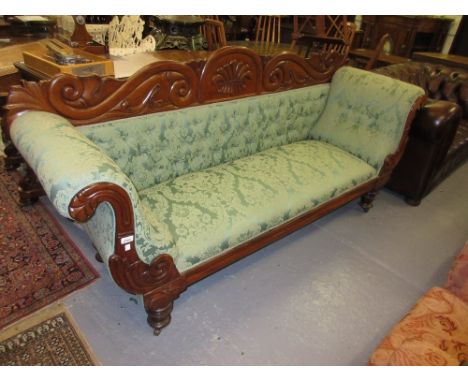 George IV mahogany and green button upholstered double scroll end sofa with a carved crested back and arms raised on turned t