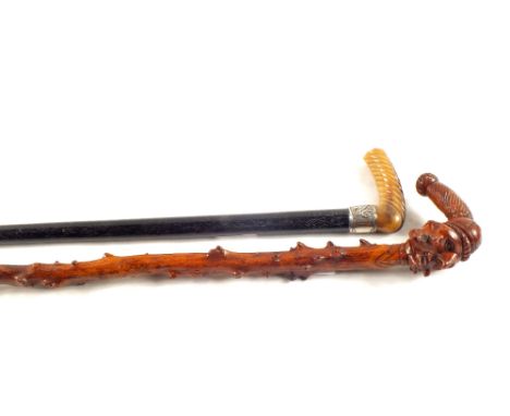 A gents walking cane with Silver band and horn grip plus a natural wooden stick with carved grotesque face grip