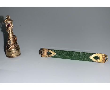 A jade coloured bar brooch with yellow metal end mounts, stamped '9'; a yellow metal lighthouse charm with garnet and pearl, 