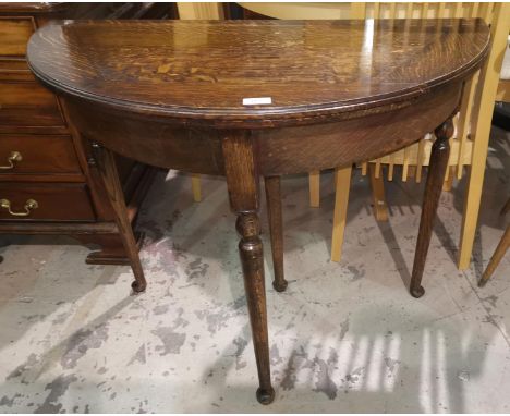 A 1930's fold-over card table with oak demi-lune top, on turned legs 