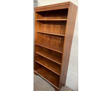 A reproduction yew bookcase with a moulded dentil cornice and shelves on bracket feet
