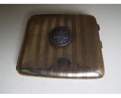 A white metal cigarette case with engine turned decoration to the front and bearing an applied plaque with eagle, swastika an