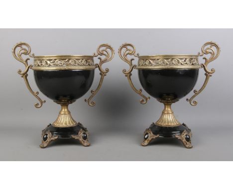 A pair of decorative black ceramic and brass mounted twin handled centerpiece urns, with pierced floral border, raised on fou