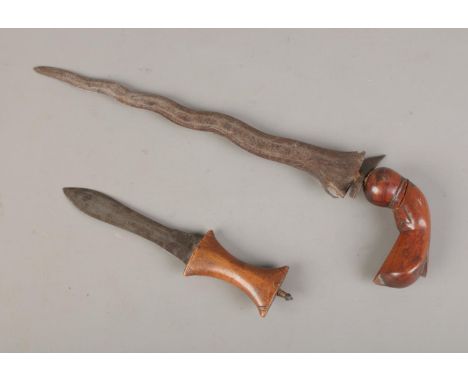 A Sudanese arm knife with a tapering straight blade and a carved wooden hilt, accompanied by a Southeast Asian Kris dagger fe