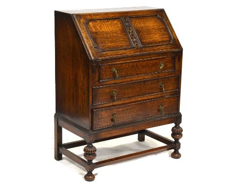 1920s oak bureau, fall front enclosing a light oak fitted interior, three long graduating drawers, turned and carved legs joi