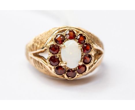 An opal and garnet dress ring, the oval opal with a stone set border,&nbsp; 9ct gold textured shank, size N 1/2, total gross 