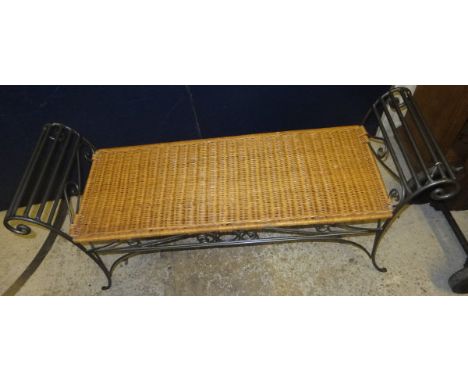 A wrought iron two seat bench with scrolled arms and wicker seat 