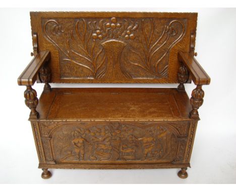An early 20th Century oak monks bench, the rectangular back carved with foliate design over a box base with hinged lid, the f