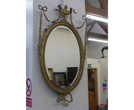 A Regency style gilded oval shaped wall mirror surmounted with an urn finial, garlands and ribbons. 