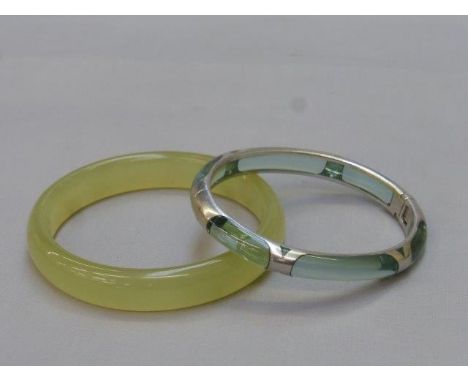 A jade bangle and a silver bangle inset with glass.