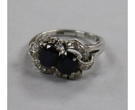 An 18ct white gold and two stone sapphire crossover ring with diamond set border, size N.