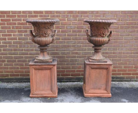 Pair of weathered cast concrete terracotta coloured campana shaped garden urns with plinths, each with a gadroon rim above an