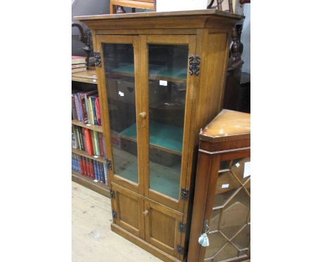 Reproduction narrow oak bookcase with a moulded cornice above two glazed and two panel doors on a plinth base, 28.5ins wide x