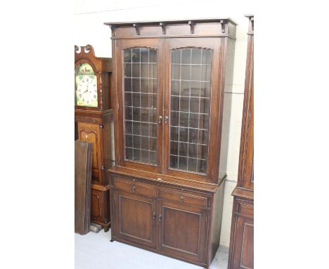 Pair of early 20th Century Arts and Crafts oak bookcases each with a shaped cornice above two lead glazed arched doors, the b