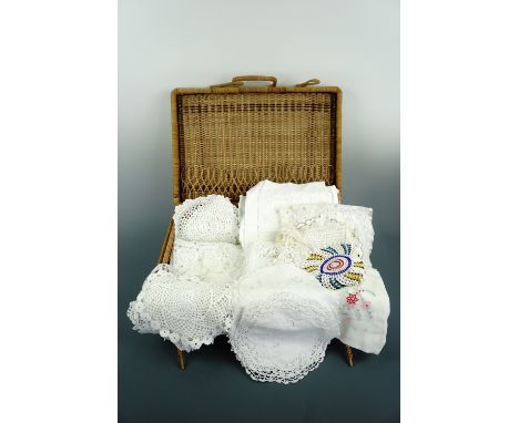 A rattan case containing antique and vintage table linens and textiles, including table cloths, decorative mats, doilies and 