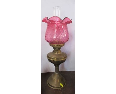 A brass oil lamp, with cranberry glass shade