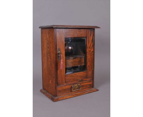 A small early 20th century oak smoker's cabinet, with a glazed panelled front and inset caddy.