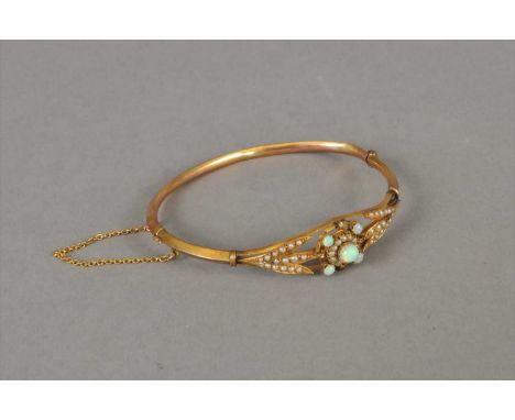 An early 20th century opal and pearl bangle, designed as a a central opal and split seed pearl cluster flanked to each side b