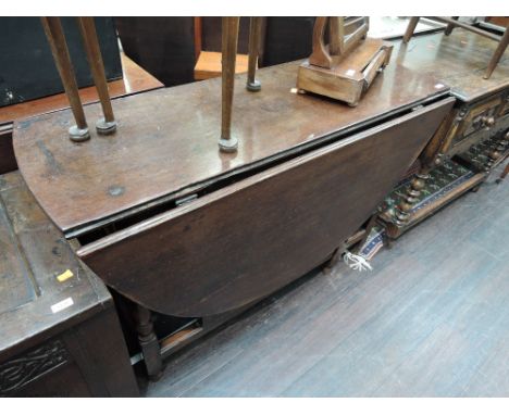 An early 20th century oak dining table in the 18th century style having oval drop leaf top on baluster gate legs