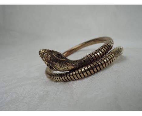 A 9ct gold snake coiled bangle having facetted ruby eyes to engraved head and steel spring to interior
