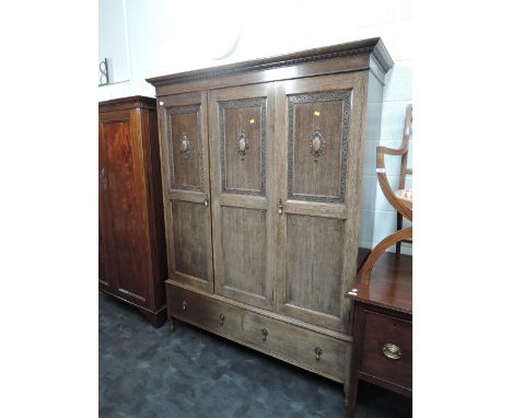 A 1920's oak triple wardrobe having applique decoration and drawer base
