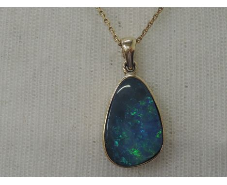 A black opal doublet pendant in a enclosed 9ct gold mount with pierced decoration to reverse on a 9ct gold chain