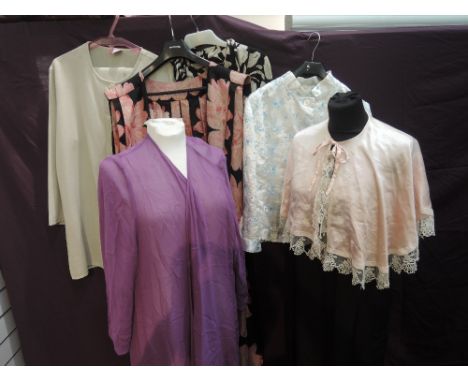 A selection of ladies clothing including pink floral sleeveless cape, black silk night gown, pink bed cape with lace decorati