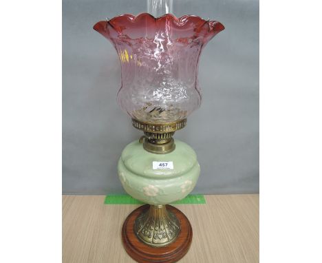 A Victorian oil lamp having later cranberry and clear glass shade on green ceramic reservoir and brass and wood base