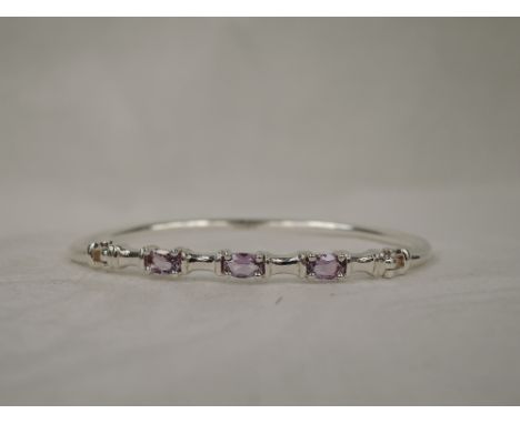 A narrow silver bangle with clip clasp set with three amethyst style stones