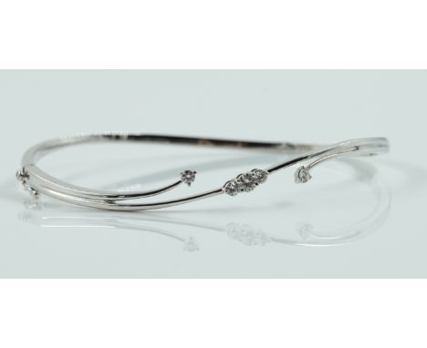 A WHITE GOLD AND DIAMOND OVAL HINGED BANGLEThe front mounted with five circular cut diamonds, detailed 750 025, on a snap cla