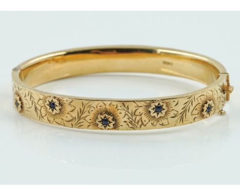 A VINTAGE GOLD BANGLE WITH SAPPHIRESThe hinged bangle half decorated with floral engraving and set with five star set blue sa