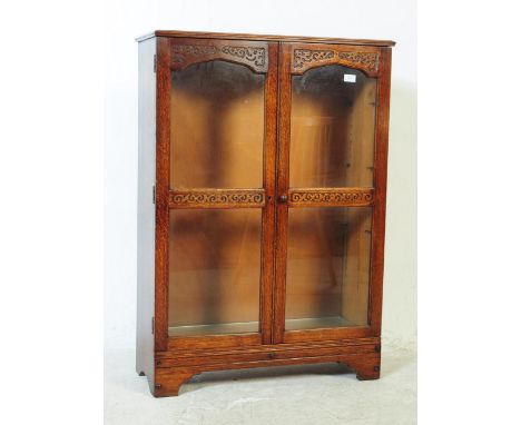 A Jacobean revival carved oak bookcase cabinet. Twin glazed door with carved detailing. Shelved interior. Flared top above wi