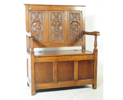 A 20th century carved oak monks settle bench. Having a large back rectangular carved panel depicting three figural heads in f