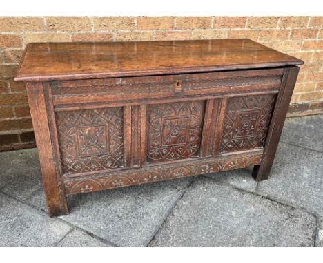 AN OAK RECTANGULAR COFFER  with candle box, carved triple panel front and on stile feet, height 65cm, width 118cm, depth 47cm