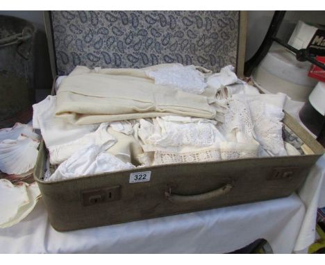 An assortment of vintage linens, household textiles and children's gowns with vintage suitcase