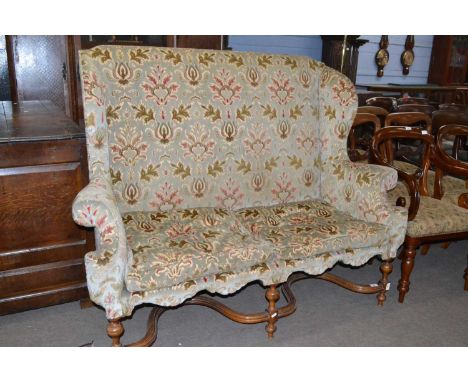 A Carolean style wing back sofa with floral upholstery and turned legs united by two X formed stretchers, 155cm wide