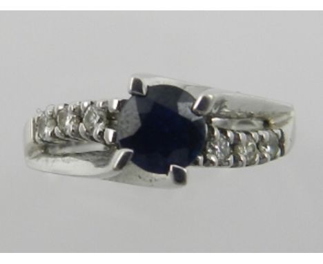 An 18 carat white gold, diamond, and sapphire set ring, the central round cut sapphire flanked by six diamonds, the shank sta