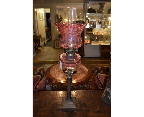 A late 19th century Corinthian column oil lamp, having a cranberry glass shade and reservoir, raised on a stepped base. H.77c
