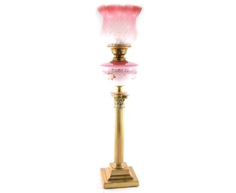 A brass Corinthian column oil lamp, pink tinted opaque shade with enamelled decoration, tinted ruby shade complete with chimn